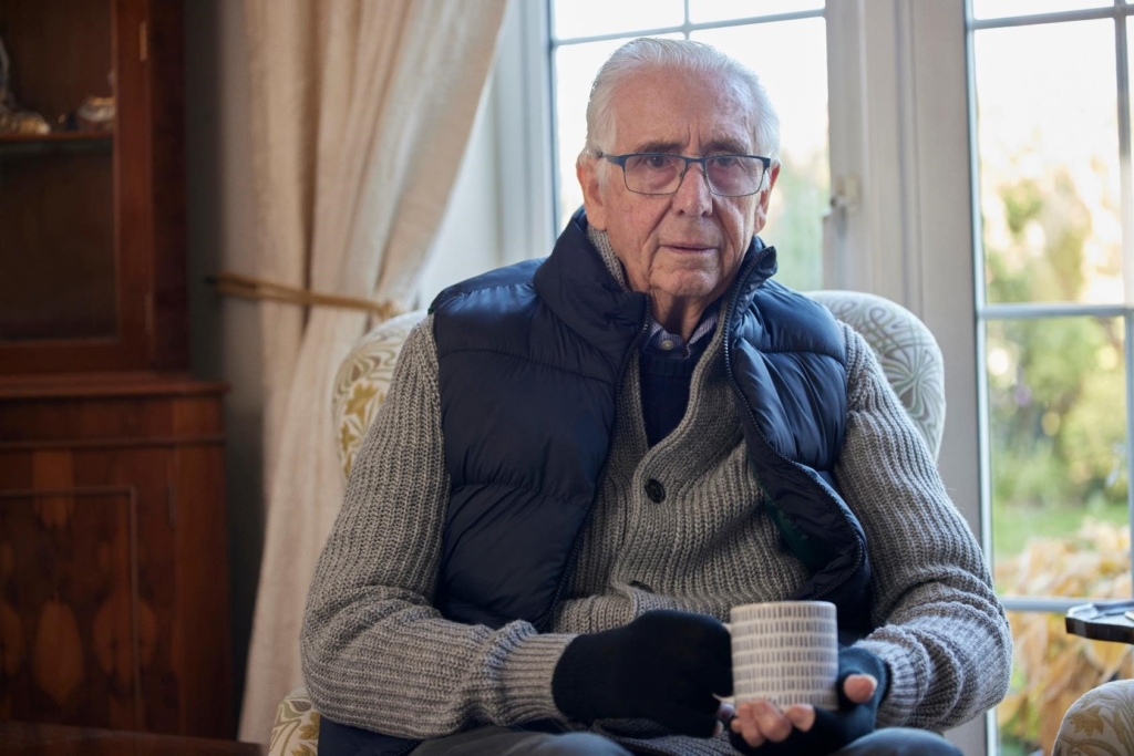 Senior feels cold, so has sweater, coat and gloves on, holding hot coffee