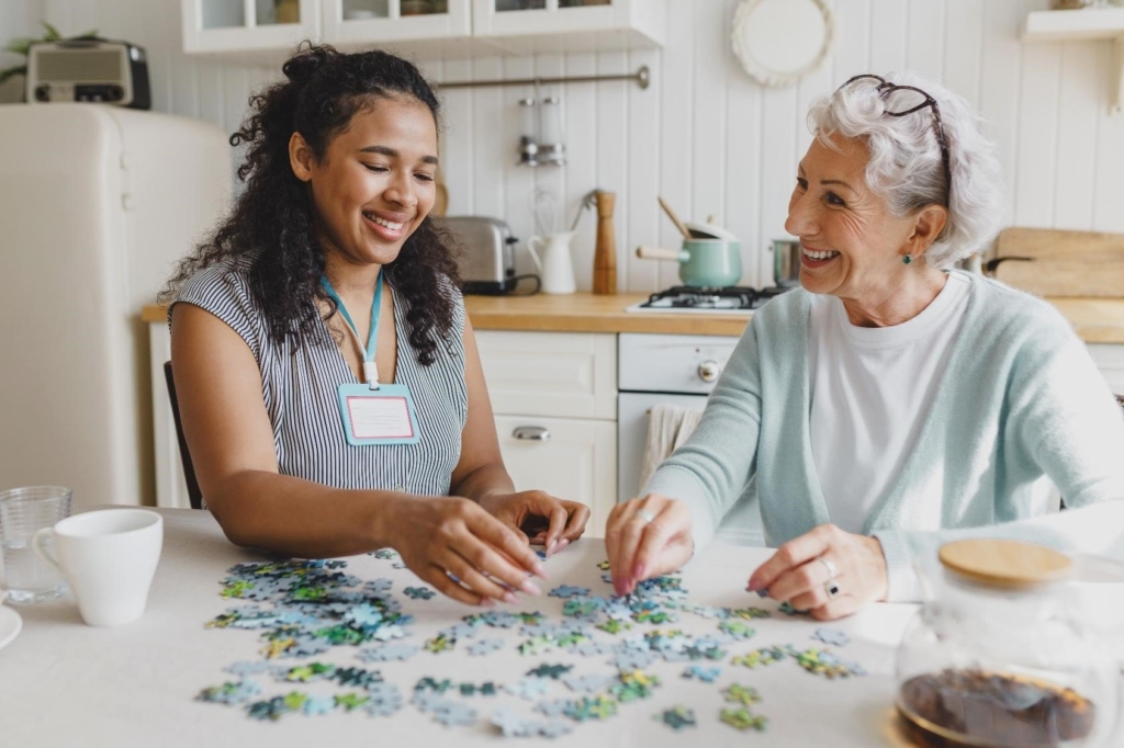 in-home care provider and older woman in kitchen holding puzzle pieces
