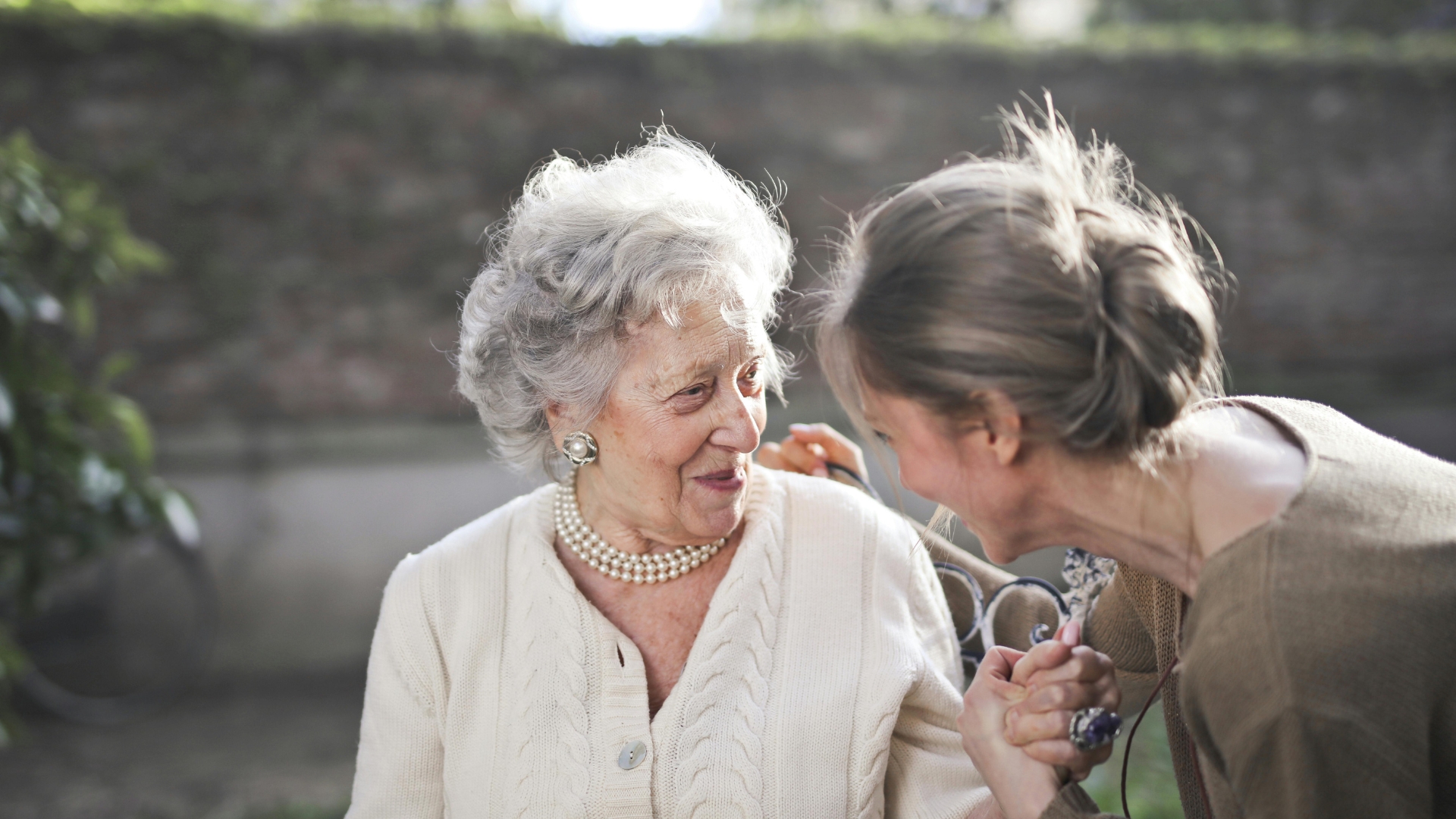 Young woman with a white hair bun talking to a senior woman with short grey hair while holding her hand outdoors
