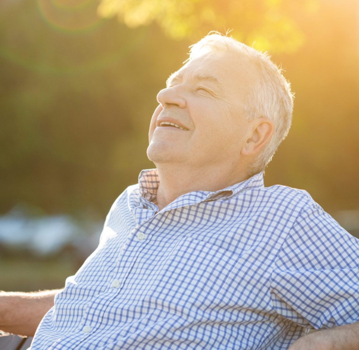 A cheerful elderly man smiling with face tilted to the sky, sitting out side on a bench at sunset. senior home care in Pleasant Hill