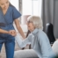 A caregiver demonstrates her caregiver skills by helping an older adult get up.