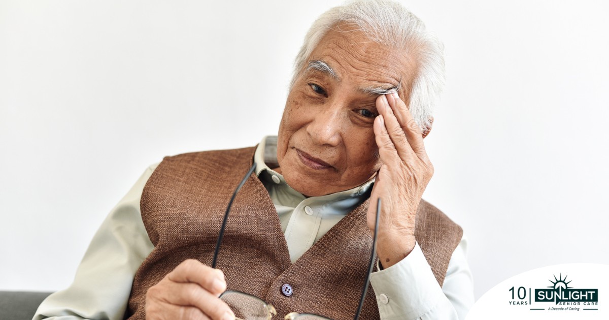 An older adult holds his head and his glasses representing vision problems like macular degeneration.