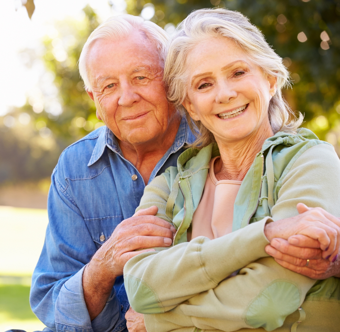 A husband and wife outside, with husband arm around wife.