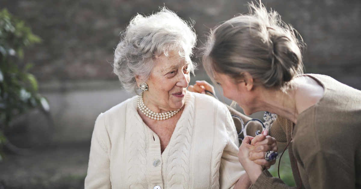An elderly woman smiling warmly while holding hands and talking with a younger woman outdoors. The scene reflects compassion and support, symbolizing quality home care in LaVista.