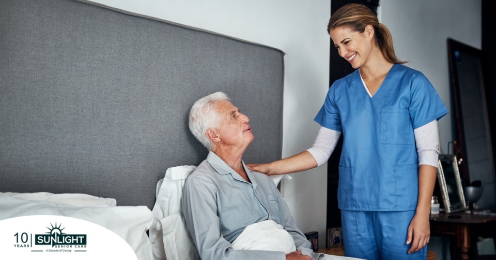 A caregiver smiles at an older client in bed, representing the compassion involved in being a live-in caregiver.