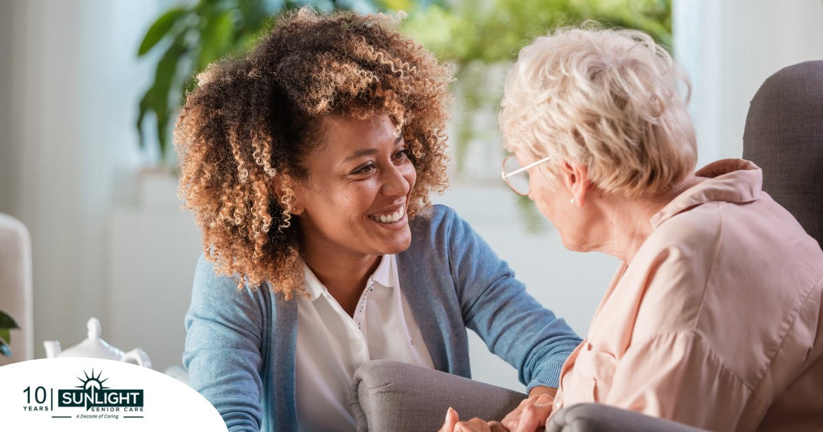 A caregiver smiles at an older client in a chair, representing the joy that can come from a healthy work-life balance.