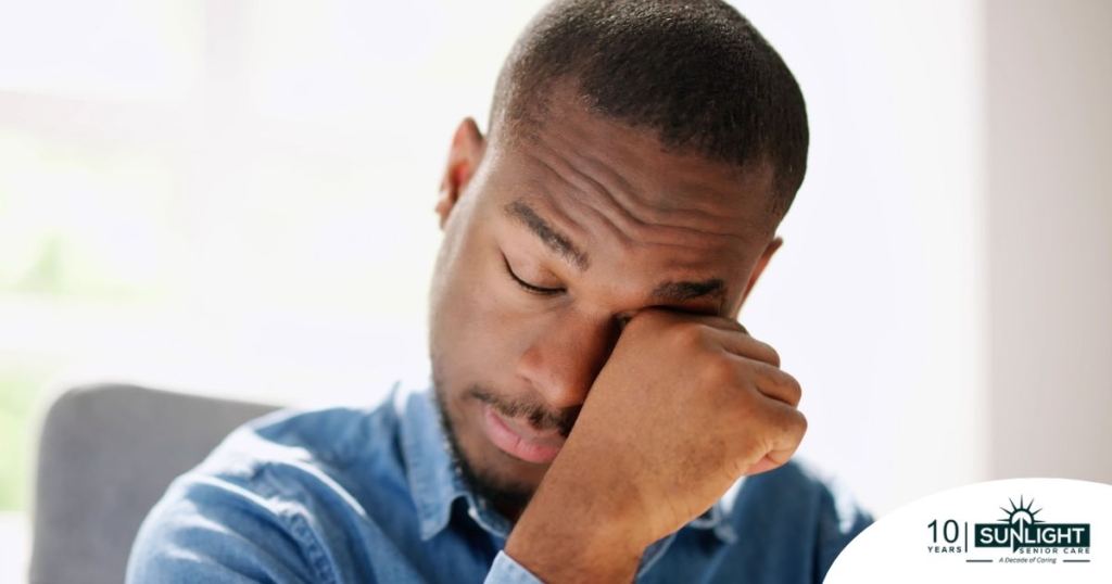A man tiredly rubs his eyes, representing the exhaustion that can come with family caregiving.