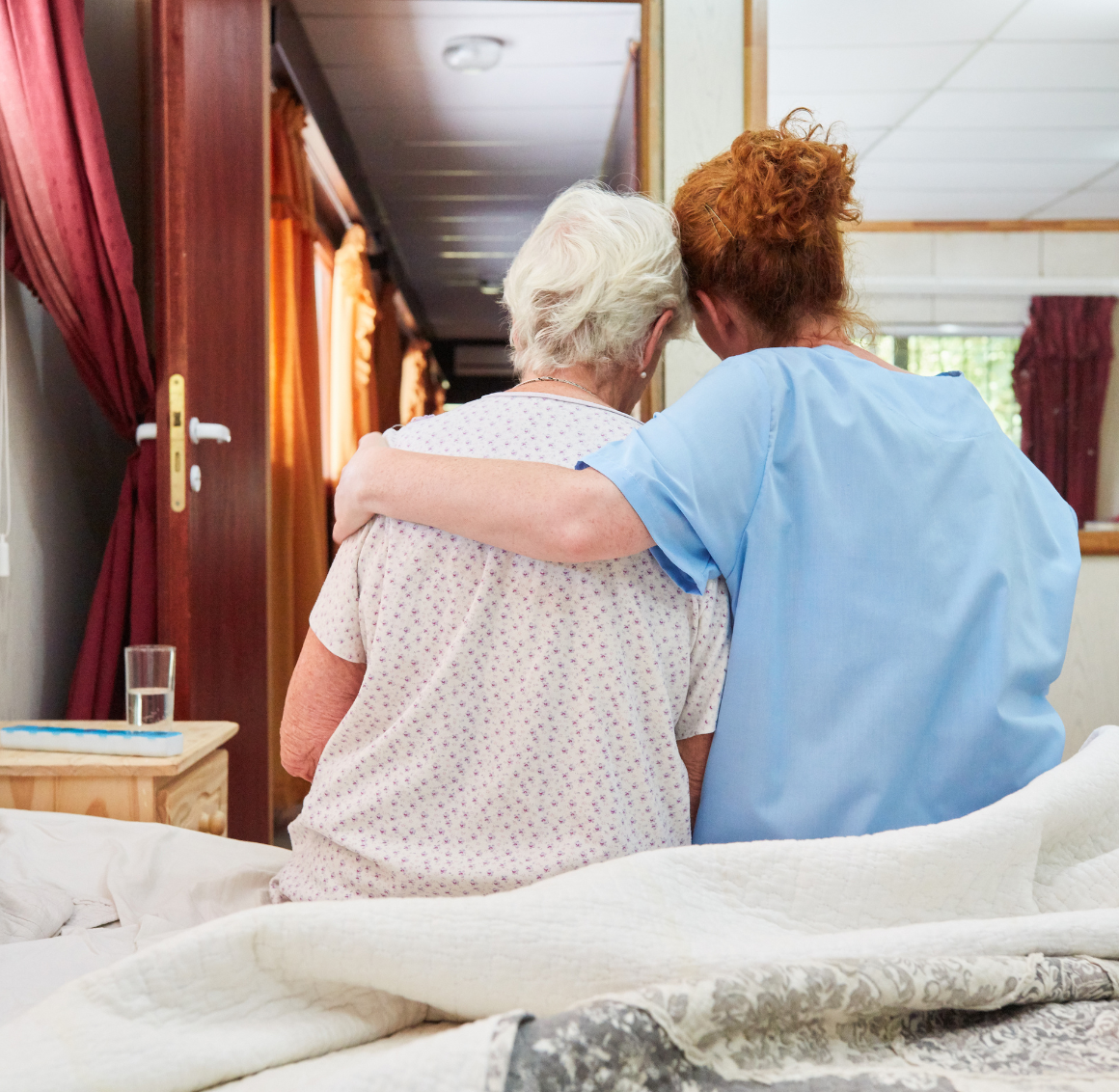 Hospice Support A caregiver gently embraces a senior while sitting together on a bed, reflecting compassionate hospice support in Des Moines.