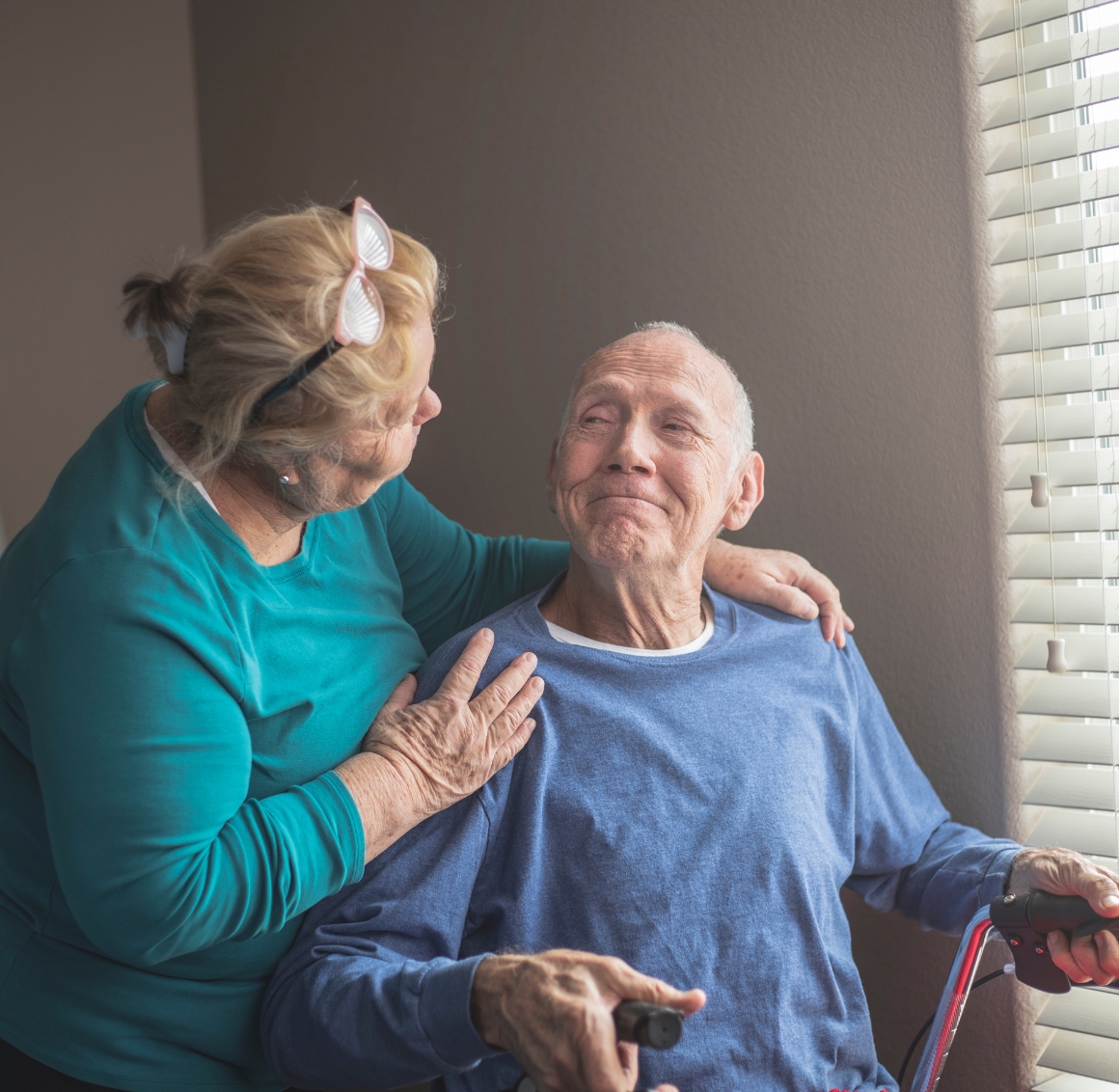 Personal Care (8) An elderly man in a wheelchair smiles at a caregiver standing beside him with a hand on his shoulder. The moment shows the compassion and support provided through Personal Care in Des Moines.