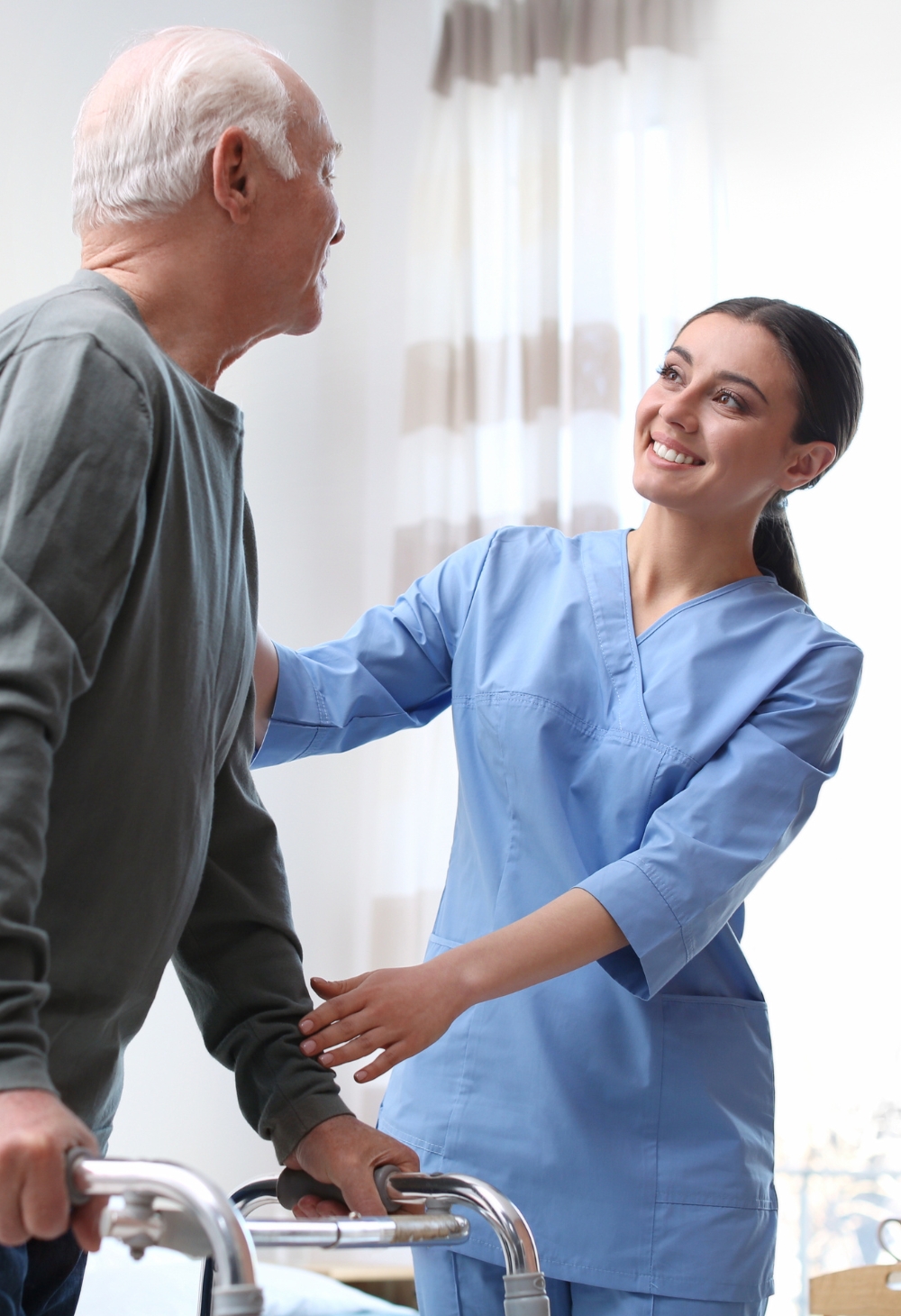 Supportive Hospice Care at Sunlight Senior Care A smiling caregiver in blue scrubs assists an elderly man using a walker, representing compassionate and supportive hospice care provided by Sunlight Senior Care in Lincoln.